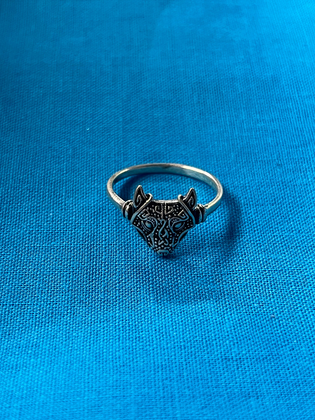 Silver ring with intricate design on a blue fabric background