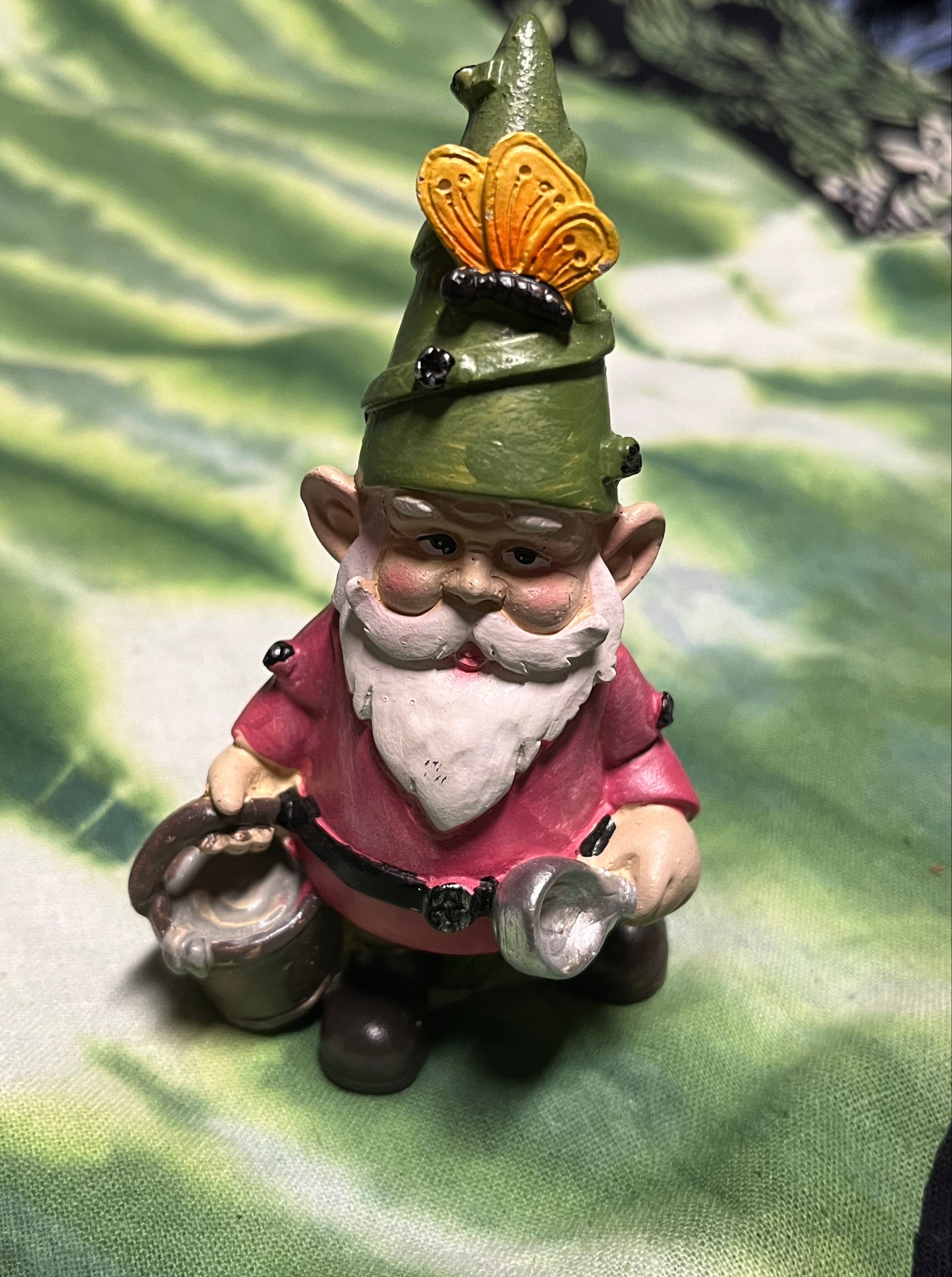 Small figurine of a gnome with a green hat and pink outfit on a textured green background