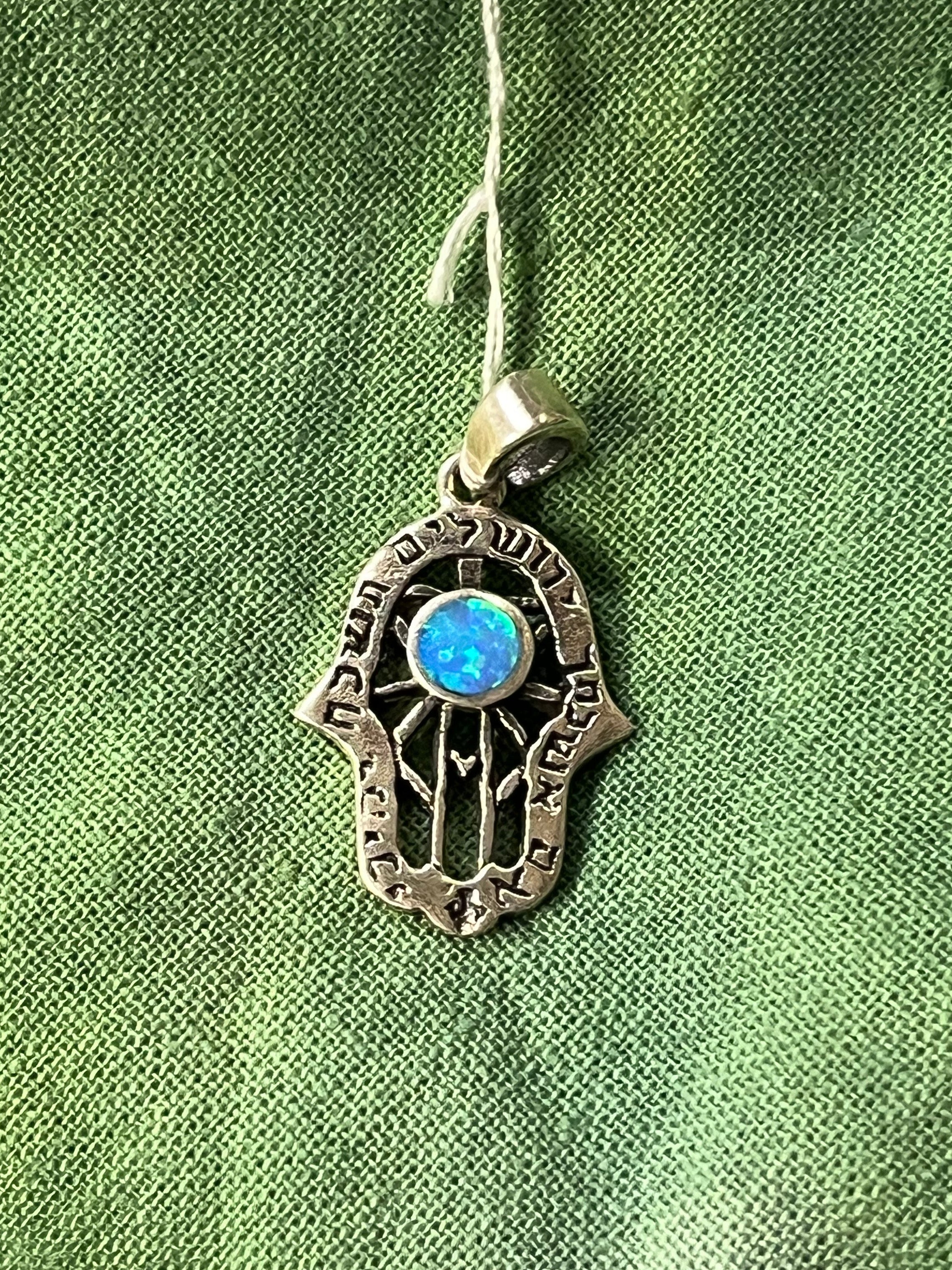 Silver Hamsa hand pendant with a blue stone on a green fabric background