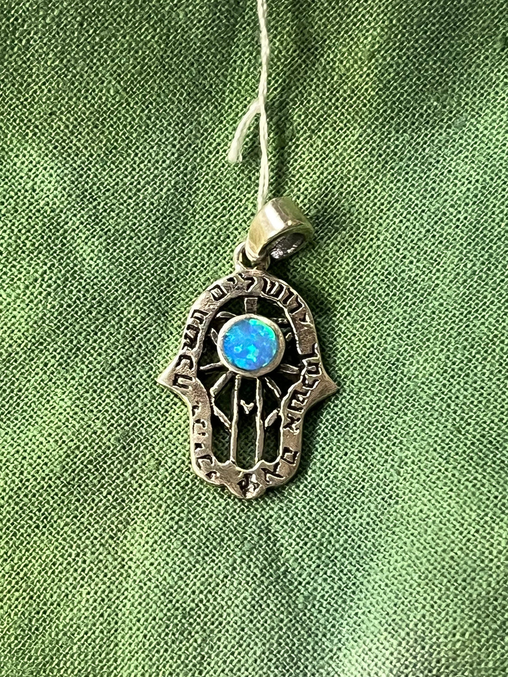 Silver Hamsa hand pendant with a blue stone on a green fabric background